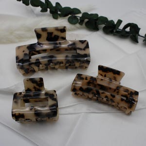 Peut inclure: Trois pinces à cheveux en écaille de tortue de différentes tailles. Les pinces sont en plastique brun et crème avec un motif marbré.