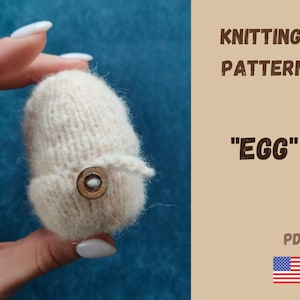 Puede incluir: Patrón de tejido para un objeto con forma de huevo. El patrón está disponible para descargar en PDF. La imagen muestra una mano sosteniendo un huevo tejido de color crema.