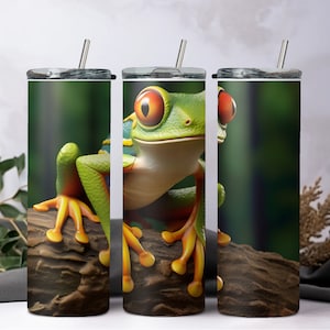 May include: Three stainless steel tumblers with a green and orange frog design. The frog is sitting on a brown log with green foliage in the background.
