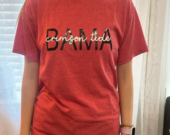 May include: Red t-shirt with the words "BAMA crimson tide" printed in black and white on the front.