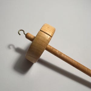 Pu&ograve; includere: Un fuso in legno con finitura naturale. Il fuso presenta un fuso rotondo, un lungo albero e un gancio in ottone. Il fuso &egrave; progettato per filare a mano filati e fibre. La venatura del legno &egrave; visibile sul fuso e sull'albero.