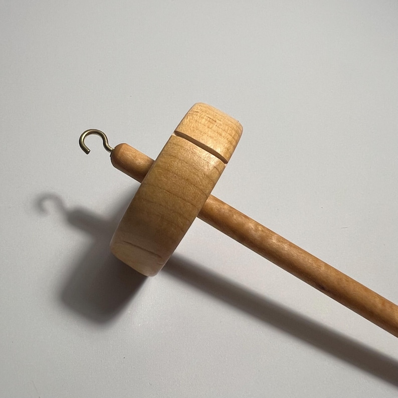 Pu&ograve; includere: Un fuso in legno con finitura naturale. Il fuso presenta un fuso rotondo, un lungo albero e un gancio in ottone. Il fuso &egrave; progettato per filare a mano filati e fibre. La venatura del legno &egrave; visibile sul fuso e sull'albero.