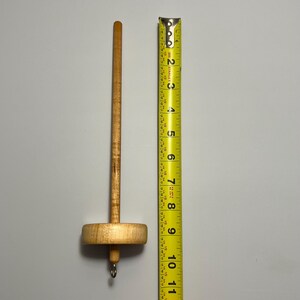 Pu&ograve; includere: Un fuso di legno per filare a mano. Il fuso &egrave; lungo circa 23 cm, con un fuso rotondo e un gancio in basso. Il legno &egrave; di colore marrone chiaro.