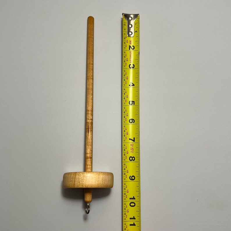 Pu&ograve; includere: Un fuso di legno per filare a mano. Il fuso &egrave; lungo circa 23 cm, con un fuso rotondo e un gancio in basso. Il legno &egrave; di colore marrone chiaro.