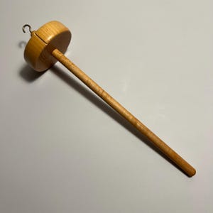 Pu&ograve; includere: Un fuso in legno con una parte superiore rotonda e un lungo fusto sottile. La parte superiore ha un gancio. Il fuso &egrave; realizzato in legno chiaro. Uno strumento tradizionale per filare a mano lana o altre fibre.