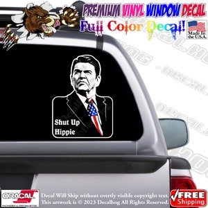 May include: A black and white decal of a man with a serious expression, wearing a suit and tie, with an American flag lapel pin. The decal says "Shut Up Hippie" in white text.