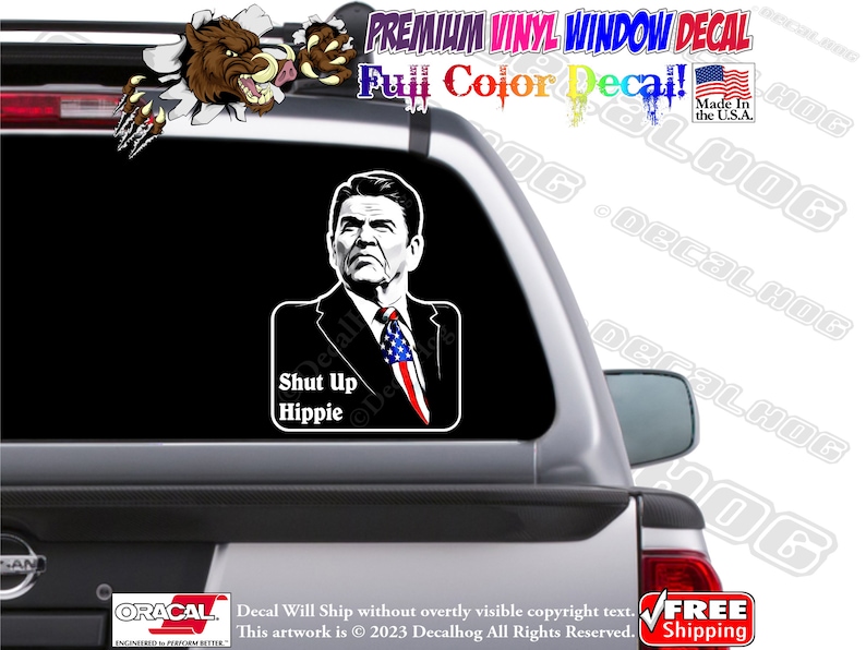 May include: A black and white decal of a man with a serious expression, wearing a suit and tie, with an American flag lapel pin. The decal says "Shut Up Hippie" in white text.