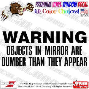 Könnte beinhalten: Ein schwarz-weißes Warnschild mit dem Text "WARNING OBJECTS IN MIRROR ARE DUMBER THAN THEY APPEAR". Das Schild ist so gestaltet, dass es aussieht, als würde ein wildes Tier durch die Wand brechen.