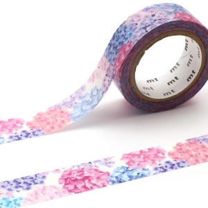 Könnte beinhalten: Eine Rolle dekoratives Washi-Tape mit einem floralen Muster aus rosa, blauen und lila Hortensienblüten. Das Klebeband ist teilweise abgerollt und zeigt das Blumenmuster sowie den Markennamen "mt" am Rand.
