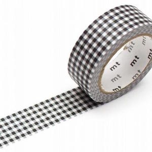 Peut inclure: Un rouleau de ruban adhésif washi à carreaux noirs et blancs, avec la marque "mt" imprimée sur le cœur. Le ruban est partiellement déroulé, révélant le motif.