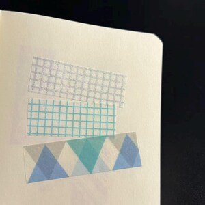 Könnte beinhalten: Drei dekorative Washi-Tape-Streifen auf weißem Hintergrund. Der obere Streifen hat ein silbernes Gittermuster, der mittlere Streifen ein blaues Gitter und der untere Streifen ein geometrisches Design mit blauen und grauen Dreiecken.