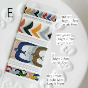Könnte beinhalten: Eine transparente Kunststoffverpackung mit dekorativen Washi-Tape-Rollen. Die Tape-Designs umfassen farbenfrohe Chevron-Muster, Vogelillustrationen und Kettenglieder-Designs. Der Text "E" ist sichtbar, zusammen mit den Abmessungen des Tapes.