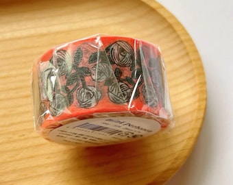 May include: A roll of decorative tape with a floral rose pattern in black and white on a red background. The tape is wrapped in clear plastic and sits on a wooden tray.
