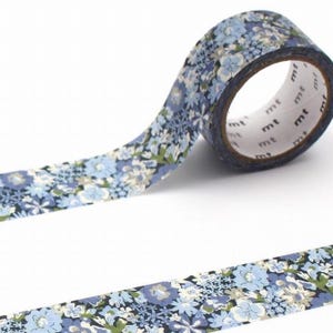 May include: A roll of patterned washi tape featuring a floral design in blue, white, and green. The tape is unrolled, revealing the pattern and the brand name "mt" on the core. This decorative tape is suitable for crafts and scrapbooking projects.