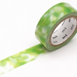Könnte beinhalten: Eine Rolle dekorativen Washi-Tapes mit einem grün-weißen Fleckenmuster. Das Klebeband ist teilweise abgerollt und zeigt einen Teil des Designs. Der Kern des Klebebands ist sichtbar, mit dem Markennamen "mt" bedruckt.