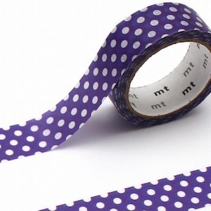 Può includere: Rotolo di nastro adesivo washi viola con pois bianchi. Il nastro è parzialmente srotolato, rivelando l'interno del rotolo con il logo "mt" stampato. Questo nastro decorativo è ideale per lavori creativi.