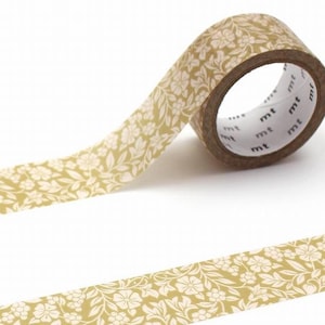 May include: A roll of decorative washi tape with a floral design. The tape has a light gold background with a repeating pattern of white flowers and leaves. The tape is partially unrolled, revealing the pattern and the brown core.