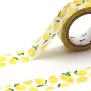Könnte beinhalten: Eine Rolle dekorativen Washi-Tapes mit einem Muster aus gelben Zitronen auf weißem Hintergrund. Das Band ist teilweise abgerollt und zeigt das Design und die Marke "mt" am Rand der Rolle. Die Zitronen sind ganz und geschnitten.