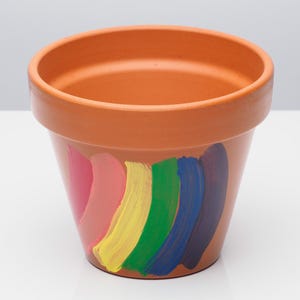 May include: A terracotta flower pot painted with a rainbow design. The rainbow is made up of pink, yellow, green, and blue stripes.