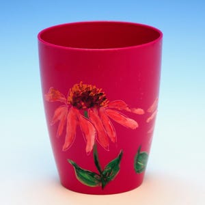 May include: A bright pink plastic cup with a hand-painted design of a pink flower with green leaves.