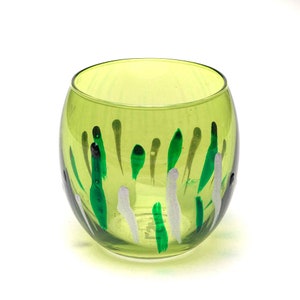 Könnte beinhalten: Ein grüner Glas-Kerzenhalter mit weißen und grünen Malereien. Der Halter ist rund und hat eine breite Öffnung oben.