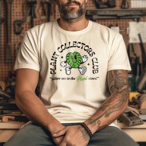 May include: A white t-shirt with a green cartoon plant character wearing a hat and holding a sign that says "PLANT COLLECTORS CLUB" and "follow me to the Plant store!"