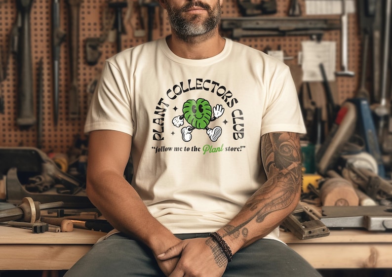 May include: A white t-shirt with a green cartoon plant character wearing a hat and holding a sign that says "PLANT COLLECTORS CLUB" and "follow me to the Plant store!"