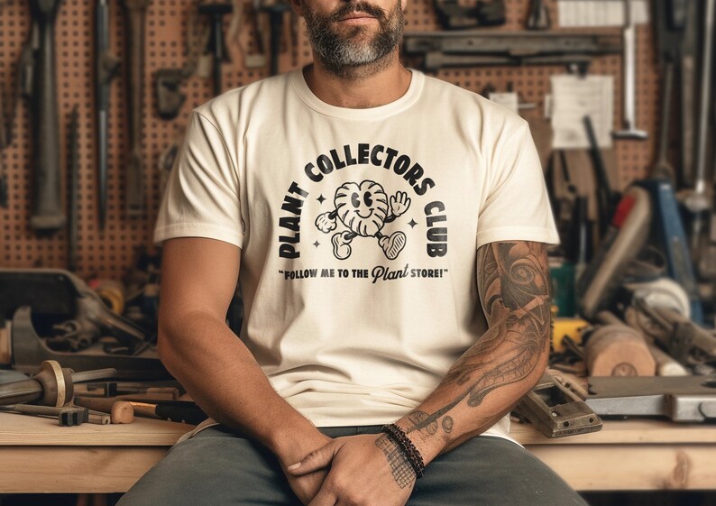 K&ouml;nnte beinhalten: Ein wei&szlig;es T-Shirt mit einem schwarzen Grafikdesign, das einen Comic-Charakter und den Text "Plant Collectors Club" und "Follow me to the Plant Store!" zeigt.