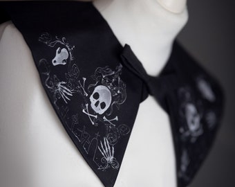 Könnte beinhalten: Schwarzer Stoffkragen mit einem weißen Totenkopf- und Knochenkreuz-Design. Der Kragen ist mit anderen weißen Skelettbildern verziert.