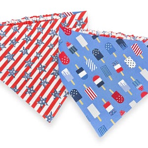May include: Two dog bandanas. One features a red and white striped pattern with blue stars. The other is light blue with various popsicle designs in red, white, and blue. Both have a ruffled edge.
