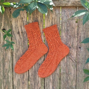 May include: A pair of orange knitted socks with a lacy pattern. The socks are laid out on a wooden surface.
