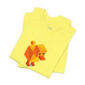 May include: Yellow t-shirt featuring a geometric duck design in orange and yellow. The duck has a square body, head, and beak. The shirt is folded and has a crew neck.