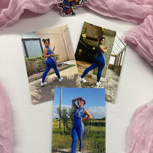 May include: An image featuring three photos of a person in a blue jumpsuit with white stripes, and a cartoon sticker of a character in a blue outfit. The photos are arranged on a white surface with pink fabric.