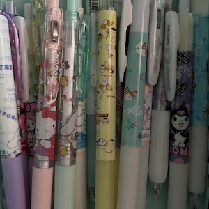 May include: A collection of colorful pens with various cartoon characters printed on them. The pens are arranged in a basket and feature characters like Hello Kitty,  Pochacco, and  Tuxedo Sam.