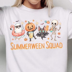 Op de afbeelding: Een wit sweatshirt met lange mouwen en een afbeelding van een geest met een flamingo-zwemband, een pompoen, een vleermuis en een skelet die drankjes en sterretjes vasthouden. De tekst "SUMMERWEEN SQUAD" staat in het oranje onder de figuren.