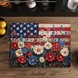 Puede incluir: Una pintura floral de la bandera estadounidense. La obra de arte presenta un campo de flores rojas, blancas y azules en lugar de las rayas y estrellas de la bandera. Las flores est&aacute;n en varias etapas de floraci&oacute;n, creando un efecto texturizado y tridimensional.
