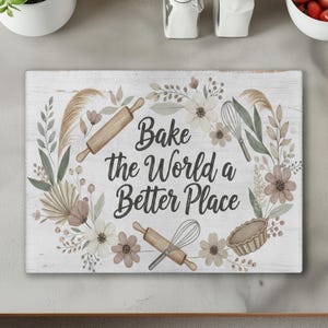 Pode incluir: Tábua de corte retangular de madeira com o texto "Bake the World a Better Place", rodeada por ilustrações florais e de pastelaria. Inclui rolo, batedor e torta.