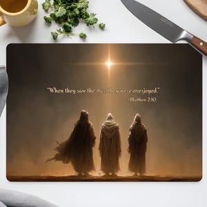 May include: Rectangular chopping board with an artistic image of three robed figures looking at a bright star. The text reads "When they saw the star, they were overjoyed." -Matthew 2:10. A yellow mug, herbs, and a knife are also visible.