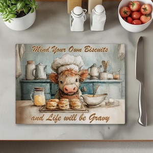 May include: A rectangular cutting board with a watercolor illustration of a cow chef. The cow is wearing a chef's hat and apron, with the text "Mind Your Own Biscuits and Life will be Gravy". The background depicts a kitchen scene.