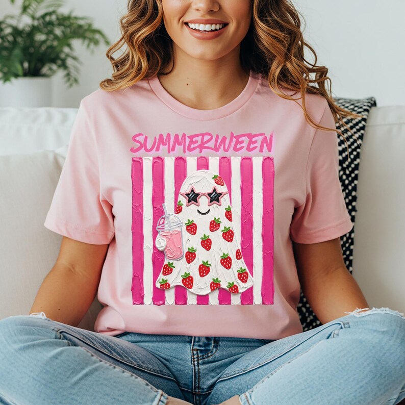 May include: Pink t-shirt with the word "SUMMERWEEN" above a ghost illustration. The ghost wears star-shaped sunglasses and is covered in strawberries. It holds a pink drink with a straw. The background has pink and white vertical stripes.