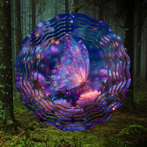 Op de afbeelding: Een decoratieve metalen windspinner met een vlinder met iriserende vleugels. De vlinder staat tegen een achtergrond van paarse en roze bloemen en een boslandschap. De spinner heeft een golvend, cirkelvormig ontwerp.