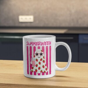May include: White ceramic mug with a whimsical "Summerween" design. The mug features a cartoon ghost wearing sunglasses and covered in strawberries, holding a pink drink. Pink and white stripes frame the text "SUMMERWEEN" at the top.