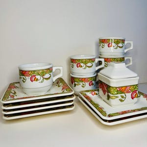 May include: A set of six white ceramic teacups and saucers with a floral pattern in shades of green, pink, and orange. The set also includes a matching sugar bowl with a lid.