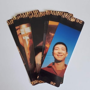 May include: A set of six bookmarks featuring a variety of images, including a man with a bright blue sky in the background, a person in a doorway, and a person with a hand raised. The bookmarks are black with a gold border and the number "26" printed on the bottom.