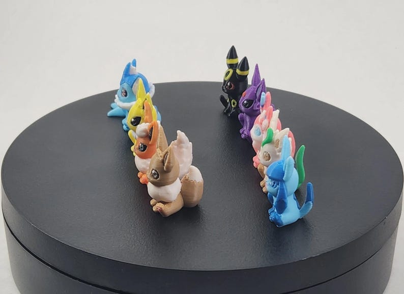 May include: A collection of colorful figurines, each depicting a unique creature. The figurines are arranged in two rows on a black circular surface. The creatures are various colors, including blue, yellow, brown, purple, pink, and green.