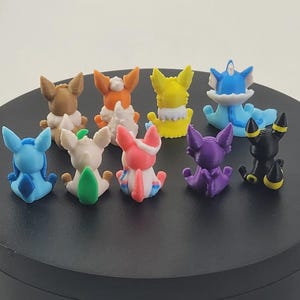 May include: A collection of colorful, small figurines of various creatures, each with unique designs and colors. The figurines are arranged on a black circular surface, showcasing a variety of characters.