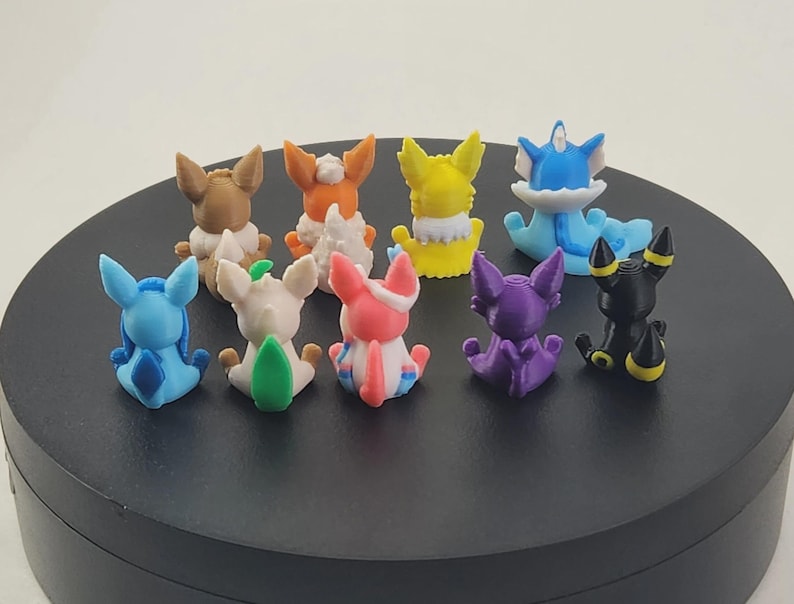 May include: A collection of colorful, small figurines of various creatures, each with unique designs and colors. The figurines are arranged on a black circular surface, showcasing a variety of characters.
