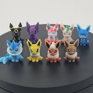 May include: A collection of colorful, small figurines of various Pok&eacute;mon characters. The figurines are in different poses and colors, including blue, yellow, purple, and brown. They are displayed on a black surface.
