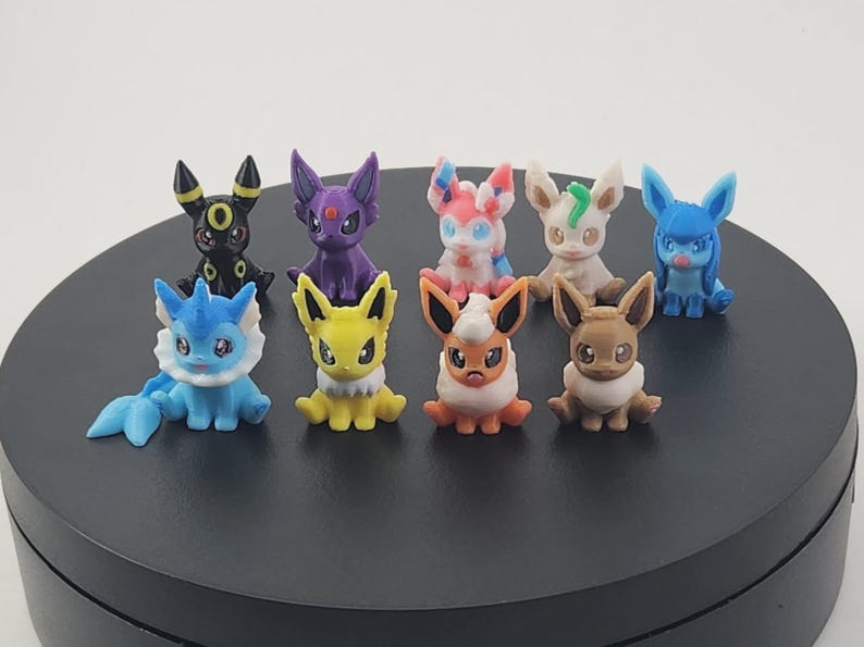 May include: A collection of colorful, small figurines of various Pok&eacute;mon characters. The figurines are in different poses and colors, including blue, yellow, purple, and brown. They are displayed on a black surface.