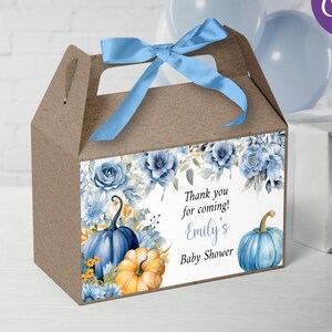 Può includere: Scatola portaconfetti con design floreale blu e giallo con un nastro blu. La scatola ha un messaggio di ringraziamento che dice "Grazie per essere venuto! Baby Shower di Emily".